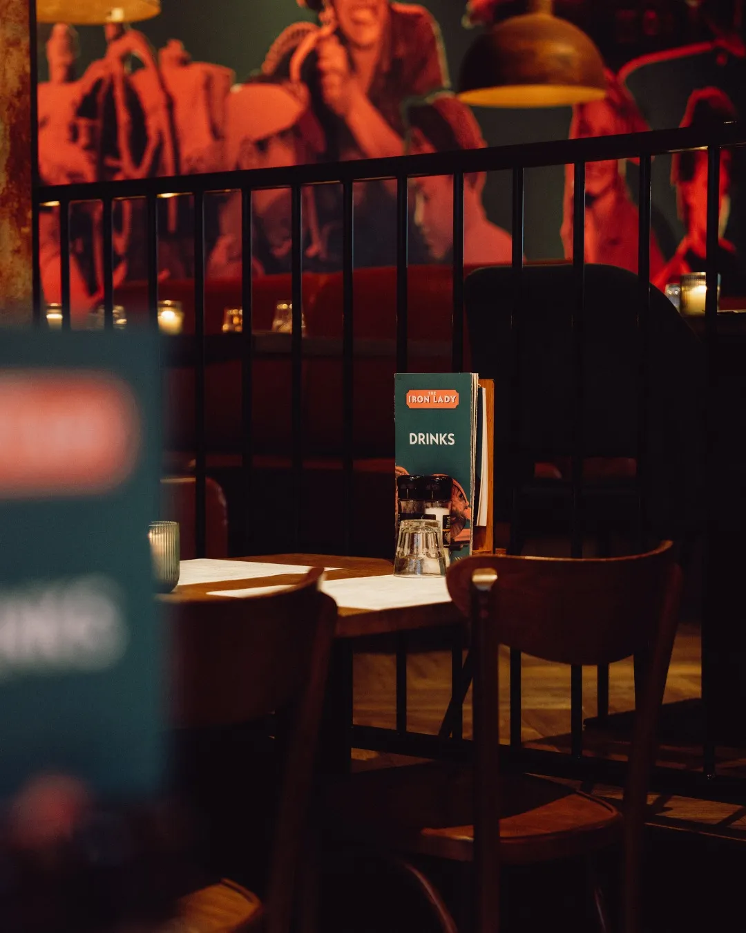 A candlelit table at The Iron Lady, the duotone mural glowing behind it
