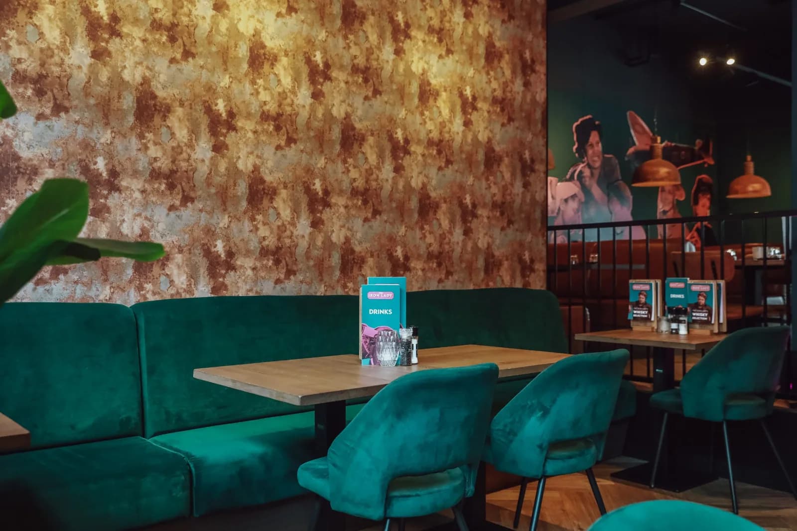 The candlelit dining room at The Iron Lady in Rotterdam — velvet-teal booths, copper and candlelight